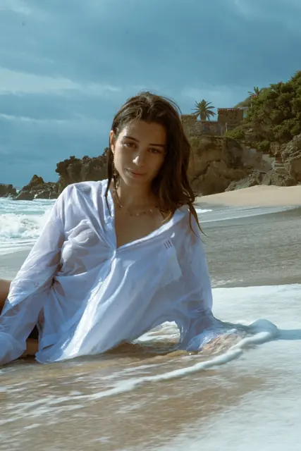 Modelo con camisa blanca sentada en el agua, sesión editorial de moda