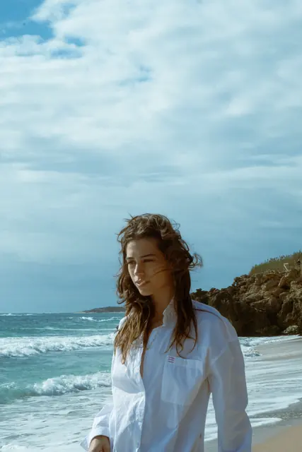 Modelo con camisa blanca en la orilla del mar, sesión editorial de moda
